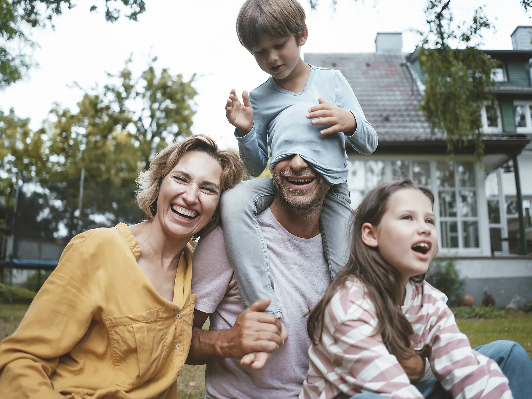 Glückliche Familie im Garten vor Haus, Kind sitzt auf Papas Schultern