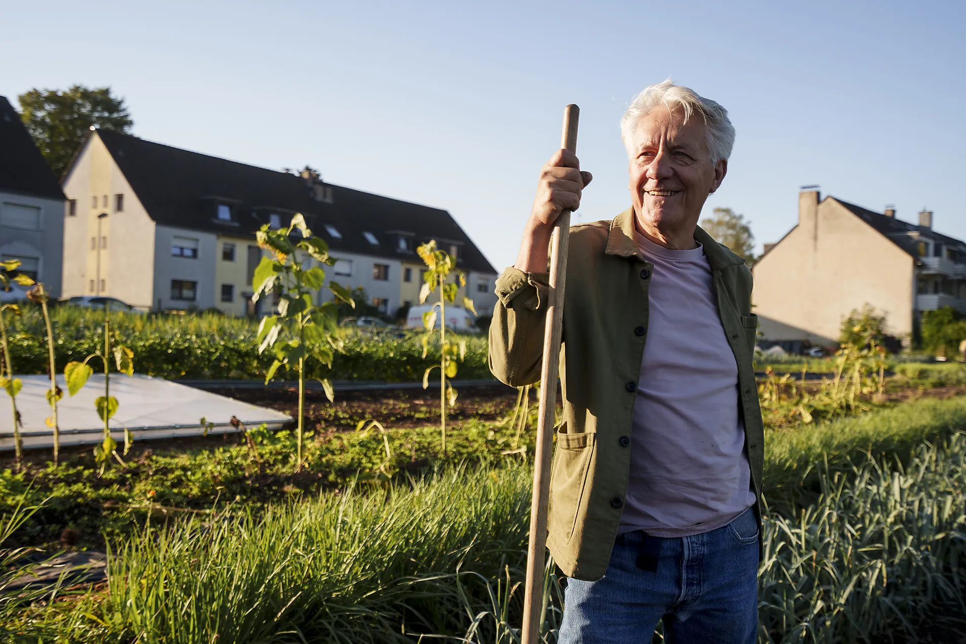 Älterer Mann mit Spaten im Gemeinschaftsgarten, Gemüsebeete vor Häusern